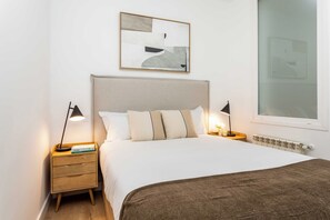 A neatly arranged bedroom with a large bed, two bedside tables, a wall-mounted abstract painting, and a window with a view. - A two-bedroom apartment with a second room for guests, set in the eclectic heart of Malasaña, steps from Tribunal and the city's vintage shops, record stores and bars. (MADRID)