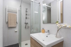A modern bathroom with a glass-enclosed shower, a white sink with a wooden cabinet, and a mirror above the sink. - A two-bedroom apartment with a second room for guests, set in the eclectic heart of Malasaña, steps from Tribunal and the city's vintage shops, record stores and bars. (MADRID)