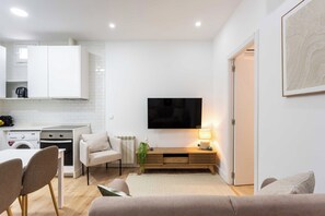 A modern kitchen with white cabinets, a built-in oven, and a washing machine. A flat-screen TV is mounted above a wooden console table with a lamp. - A two-bedroom apartment with a second room for guests, set in the eclectic heart of Malasaña, steps from Tribunal and the city's vintage shops, record stores and bars. (MADRID)