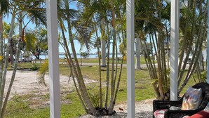 Uma área de estar coberta ao ar livre, com móveis de vime e vista para a praia e palmeiras.