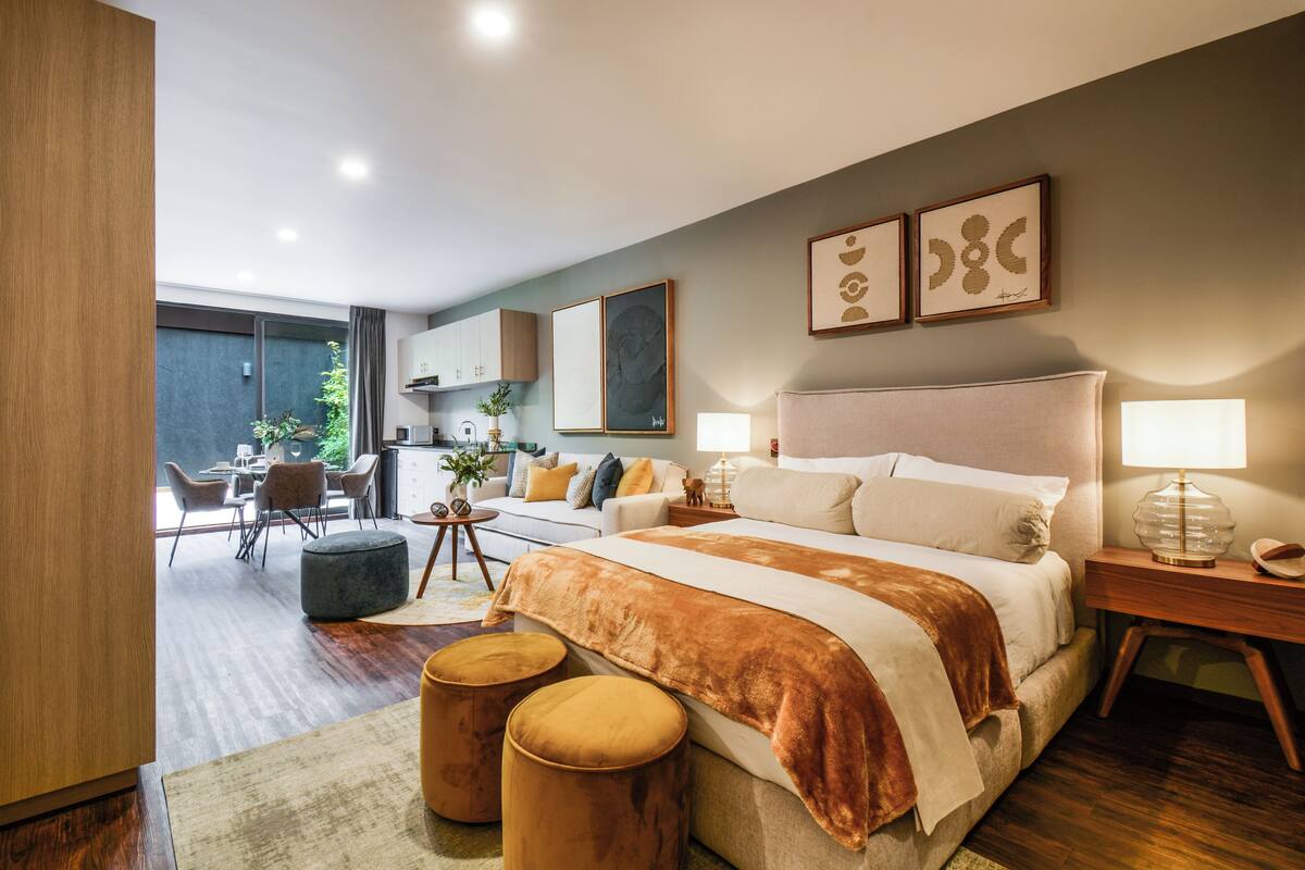 A modern bedroom with a large bed, bedside tables, a desk, and a dining area.