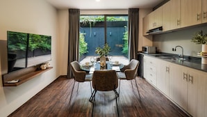 A modern kitchen with a dining area, wooden cabinets, a built-in oven, and a large window with a view of greenery. - The Sterling Condesa (Mexico City)