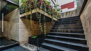 A staircase with black steps leading up to a landing, surrounded by a stone wall and a planter with various plants. - The Sterling Condesa (Mexico City)