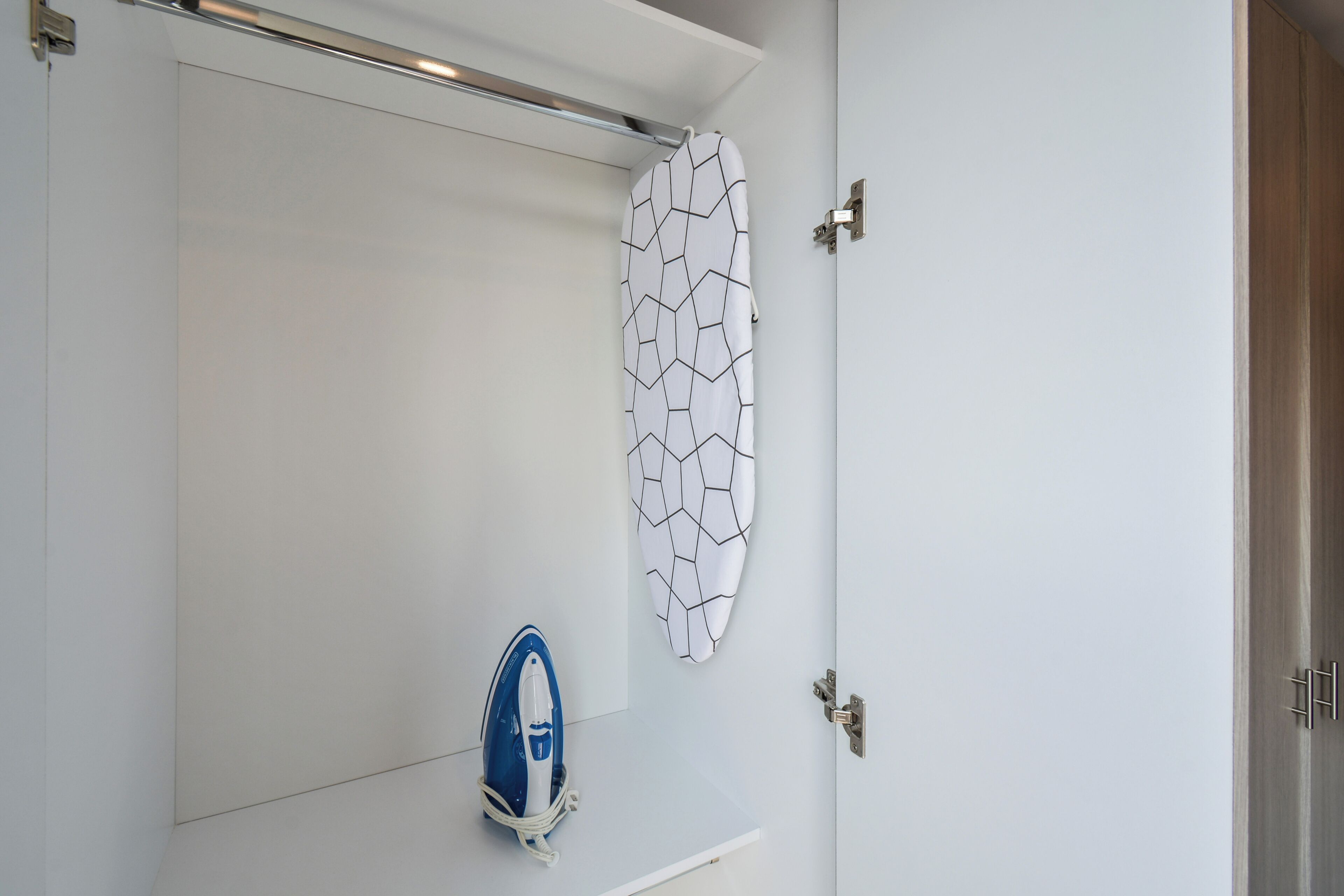 A bathroom with a white shower curtain, a white wall with a geometric pattern, and a blue and white iron on a small shelf.