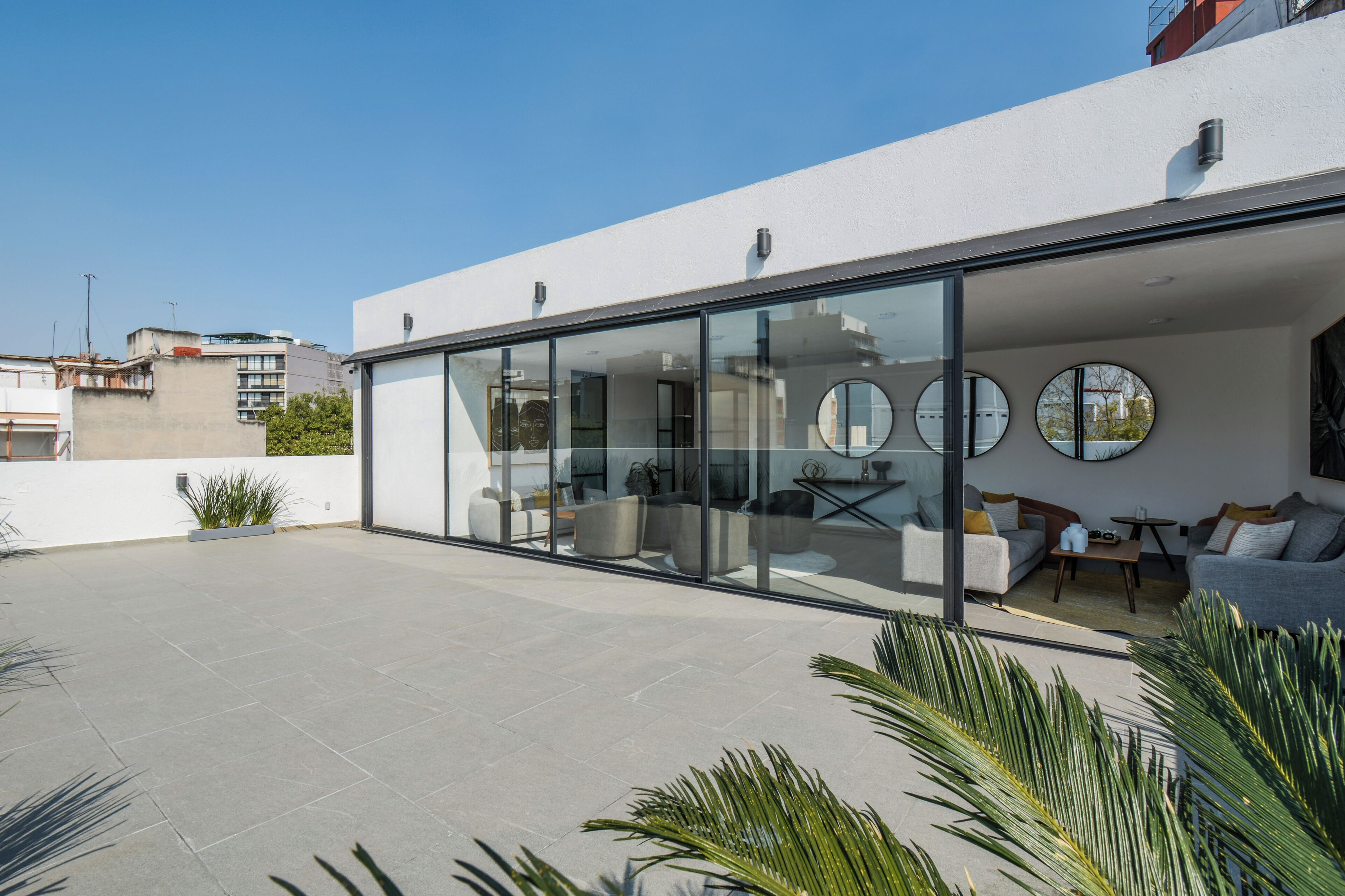 A modern outdoor living area with a glass wall, outdoor furniture, and a view of the city.