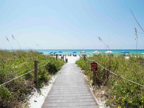 A wooden boardwalk leading to a beach with blue umbrellas and beach chairs. - Dunes of Panama #C503 | Gulf Front + Amenities (Panama City Beach)