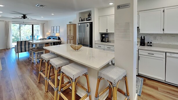 Una cucina moderna con mobili bianchi, un'isola centrale con sgabelli, un frigorifero e un'area pranzo con tavolo e sedie.