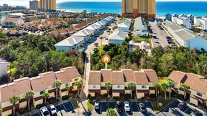Una zona turistica con accesso alla spiaggia, caratterizzata da una combinazione di edifici a bungalow e palazzi a più piani, un parcheggio e vista sull'oceano.