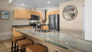 A modern kitchen with wooden cabinets, a stainless steel refrigerator, a microwave, and a marble island with bar stools. - Puu Poa 102 - Private and Serene 2/2 with ocean views (Princeville)