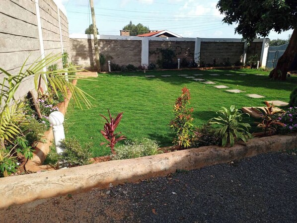 A well-maintained lawn with a stone border, various plants, and a building in the background.