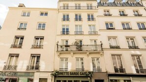 A row of multi-story buildings with balconies, a café named 'Ginette Garde Café' on the ground floor, and various storefronts. - A BLEND OF CLASSIC PARISIAN CHARM WITH MODERN SOPHISTICATION NEXT TO THE LOUVRE (Paris)