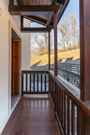 A wooden balcony with a stone wall and railing, overlooking a grassy area with trees and a clear sky. - Casa Tre Corone, on the road to Cortina d Ampezzo (Borca di Cadore)