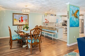 A dining area with a wooden table and chairs, a chandelier, and a painting of a beach scene. - Casa Bella - 4 bedroom, Gulf View, Cargo Lift, Outdoor Bar, Fenced Yard, (Crystal Beach)