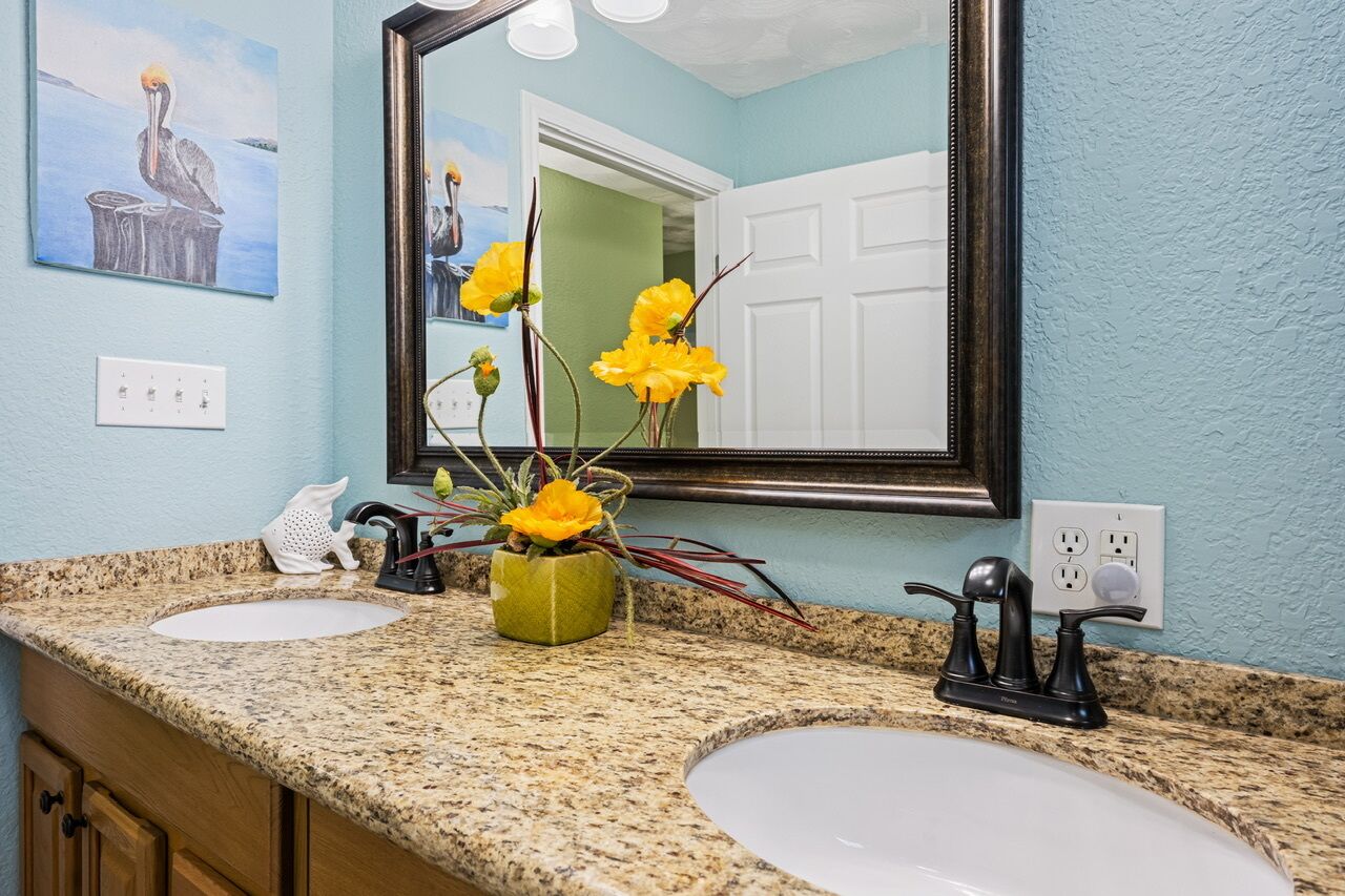 A bathroom with two sinks, a mirror, and a vase with yellow flowers.