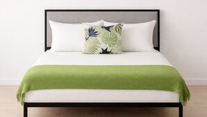 Una cama con un edredón verde, almohadas blancas y un cojín estampado con motivos florales.
