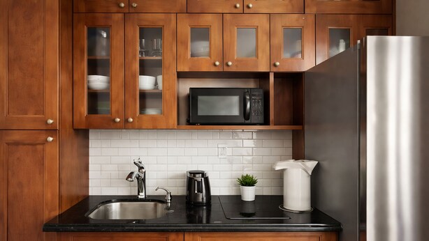 Una cocina con armarios de madera, un refrigerador de acero inoxidable, un microondas negro, un lavamanos y una cafetera.