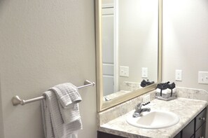 Une salle de bain avec un lavabo blanc, un miroir et un porte-serviettes sur lequel est posée une serviette blanche.