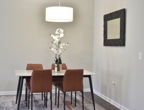 Un coin repas comprenant une table, des chaises, un vase de fleurs, un luminaire suspendu et un tableau encadré au mur.