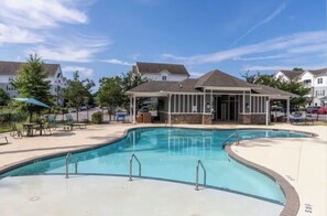 Une piscine avec un espace de détente, entourée de maisons.