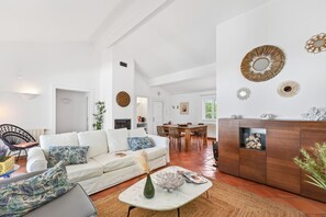 Ein großzügiger Wohnbereich mit einem weißen Sofa, einem Esstisch und einer Küche im Hintergrund.