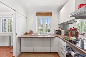 Eine moderne Küche mit weißen Schränken, einer Holzarbeitsplatte, einem eingebauten Backofen und einem Fenster mit Blick auf Grünflächen.
