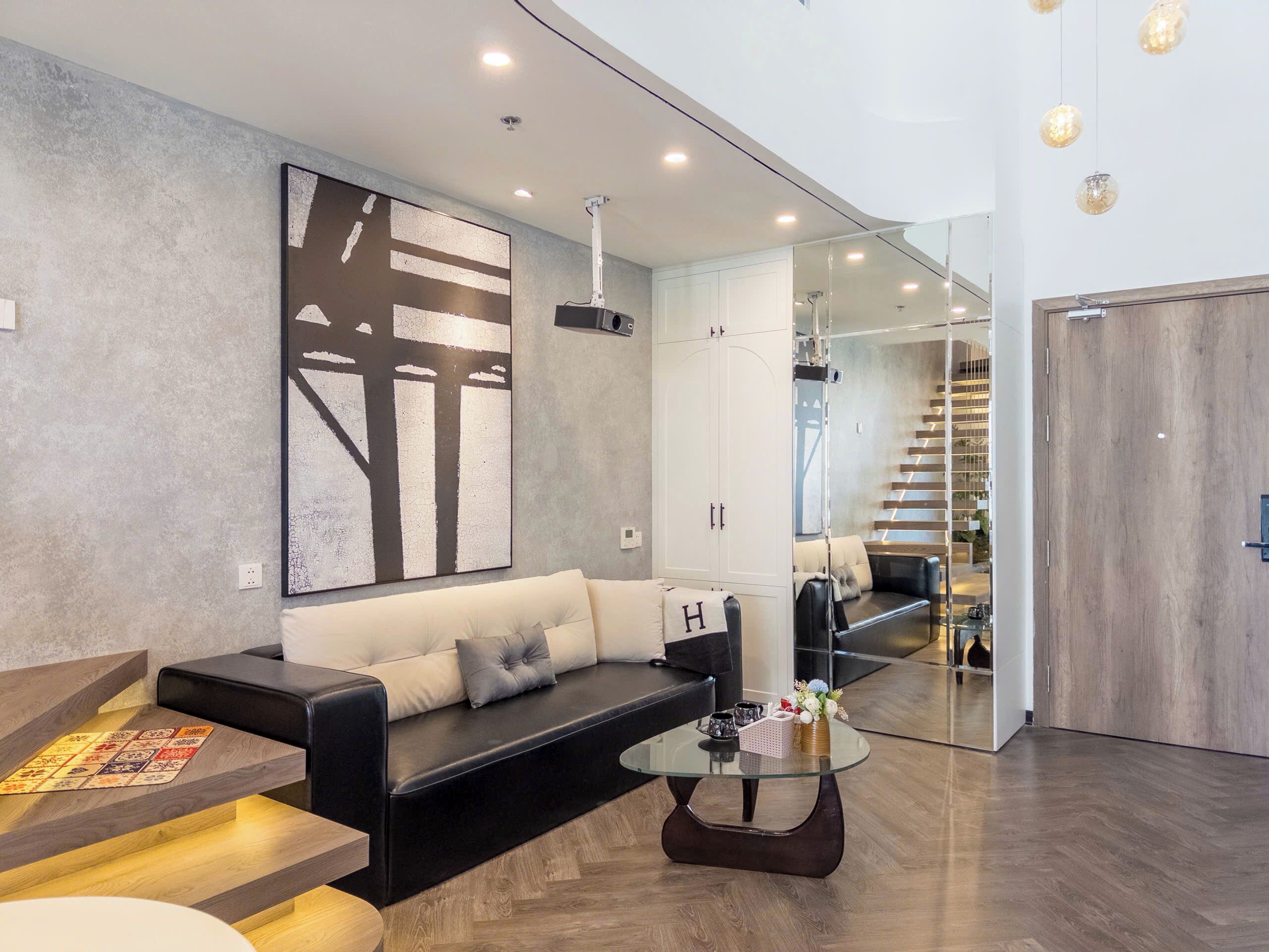 A modern living room with a black leather sofa, a glass coffee table, and a large abstract painting on the wall.