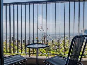 Un balcon doté d’une rambarde en métal, deux chaises noires en tissu grillagé, une petite table ronde et une vue sur le paysage urbain.