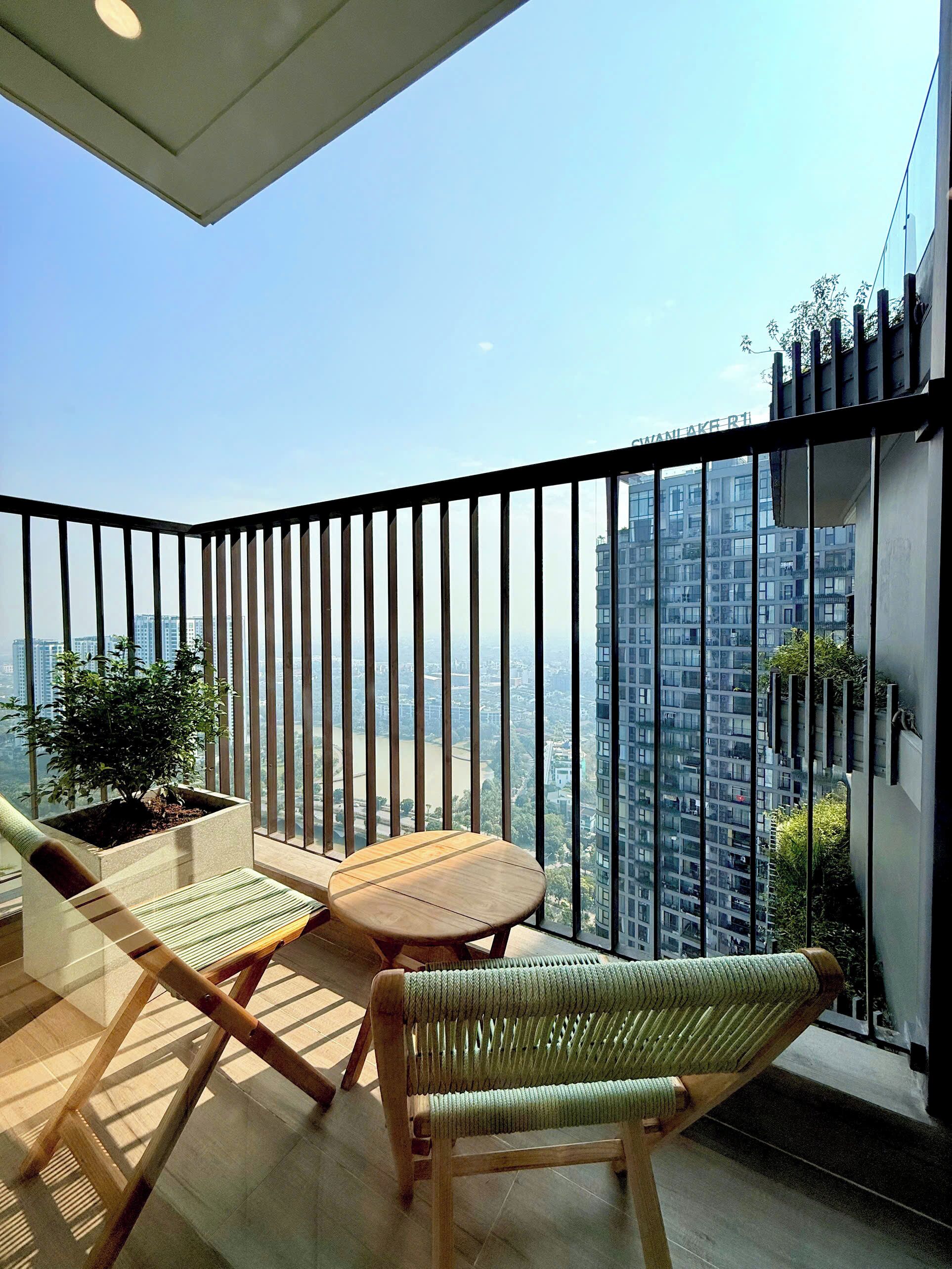 Ein Balkon mit Tisch und zwei Stühlen, einem Blumentopf und Blick auf hohe Gebäude.