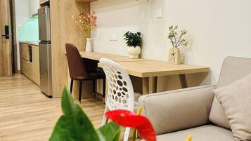 A modern kitchen with wooden cabinets, a stainless steel refrigerator, and a dining area with a white chair and a beige sofa.