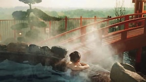 A hot spring bath with a wooden bridge and a view of trees and hills.