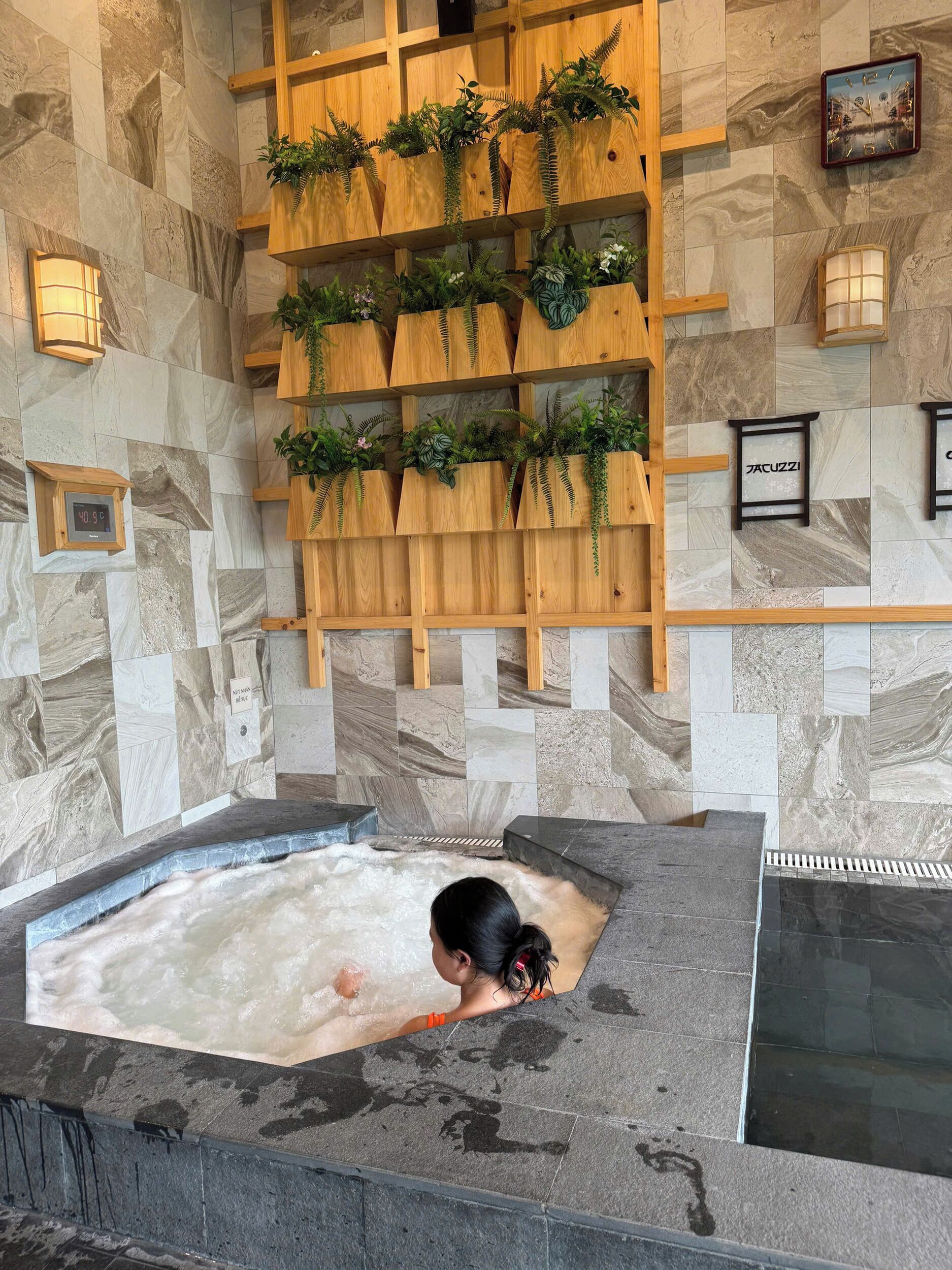 Ein Spa-Bereich mit Whirlpool, Holzregalen mit Pflanzen und einer Marmorwand.