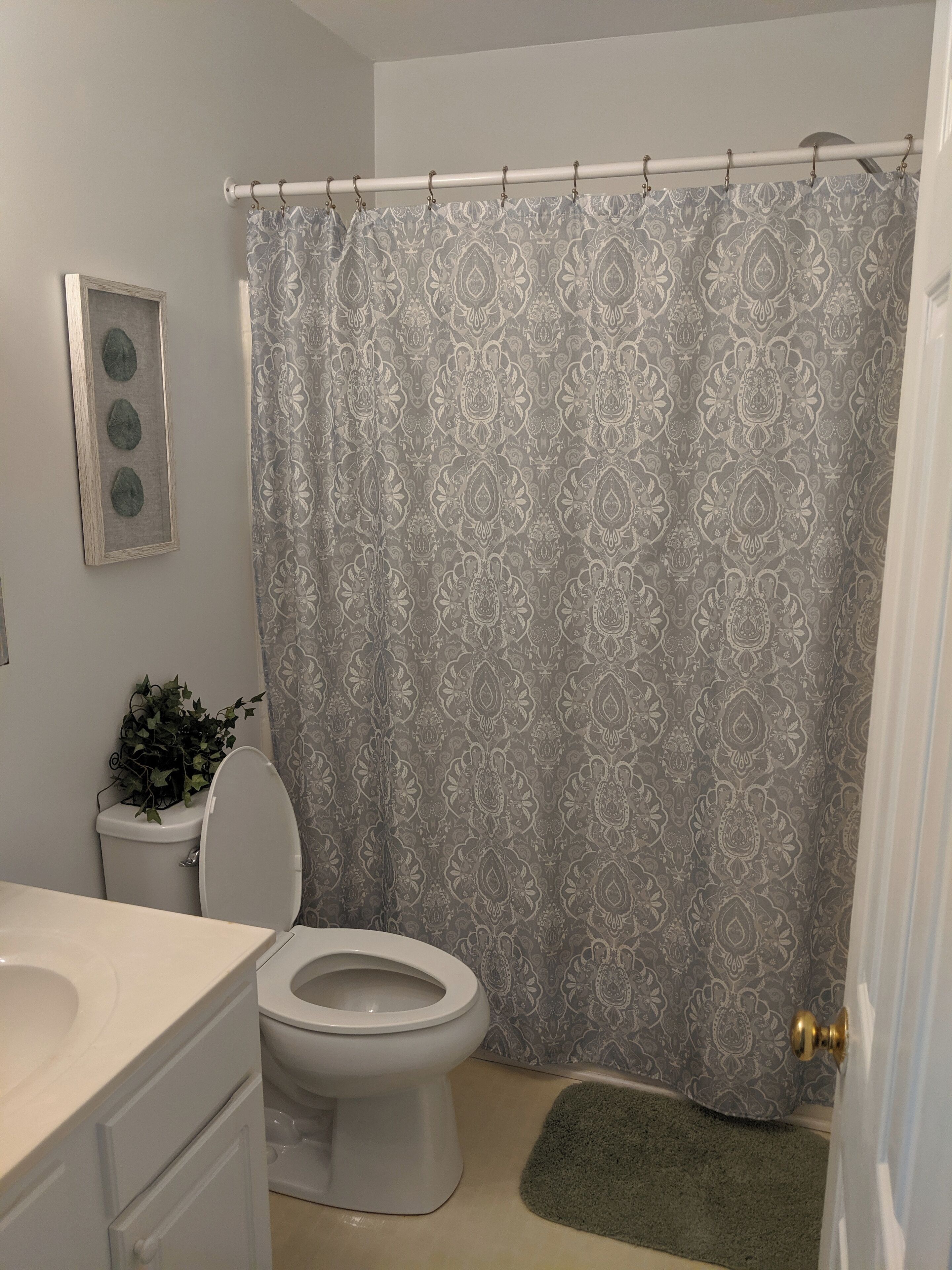 A bathroom with a toilet, a sink, a shower curtain, and a small green rug.