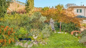 Un jardín con un puente de piedra, una pequeña construcción de madera y un muro de piedra.
