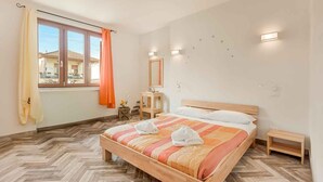 Habitación de hotel con cama de madera, una mesita de noche pequeña, cortinas en la ventana y vistas a edificios.