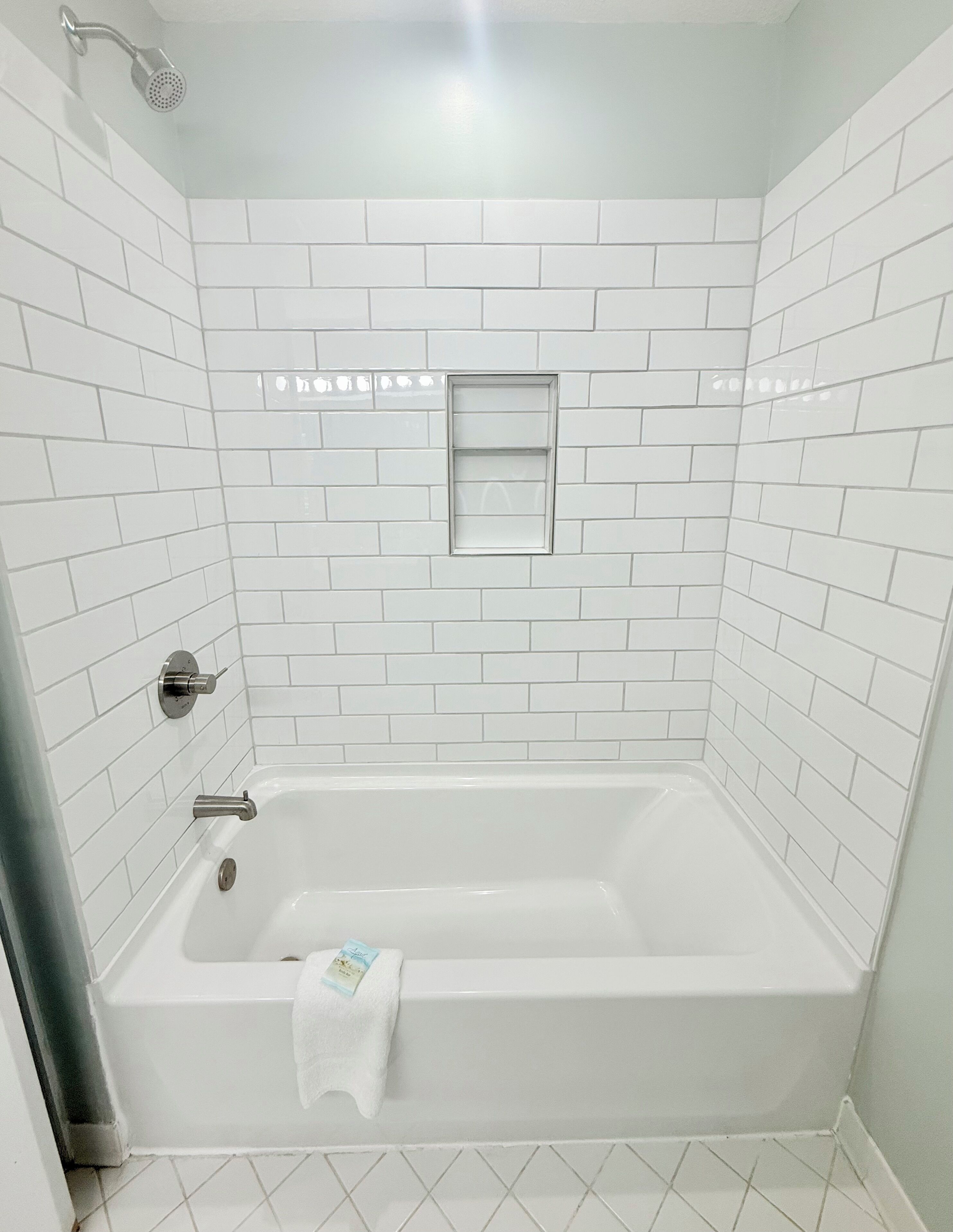 A modern bathroom with white subway tiles, a built-in window, a bathtub, and a showerhead.