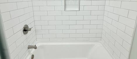 A modern bathroom with white subway tiles, a built-in window, a bathtub, and a showerhead.