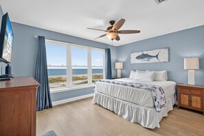 A bedroom with a large window, a ceiling fan, a bed with white bedding, a wooden nightstand, and a wall-mounted artwork. - 🌴 Gulf Front Home - Private Pool - Sweet Retreat 🌴 (Indian Pass)