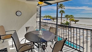 Ein Balkon mit Tisch und Stühlen, einem Deckenventilator und Blick auf den Strand und Palmen.