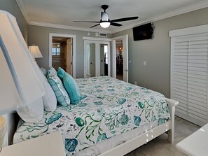 A bedroom with a bed, a ceiling fan, a TV, and a door leading to another room. - Carlos Pointe 121 | Stylish Retreat  w/Gulf Views, Balcony + Community Pool (Fort Myers Beach)