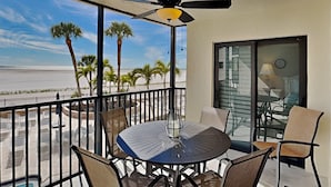 Ein Balkon mit rundem Tisch und Stühlen, einem Deckenventilator und Blick auf den Strand und Palmen.