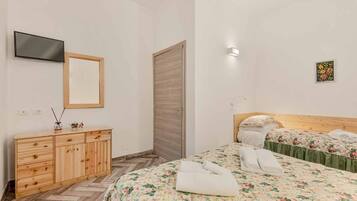 Ein Hotelzimmer mit einem hölzernen Schminktisch, einem an der Wand montierten Fernseher, einem Bett mit floralem Bettzeug und einer kleinen Wandleuchte.