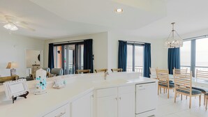 A modern kitchen with a central island, a dining area with wooden chairs, and large windows with curtains. - 204E A Beautiful 3 bedroom/3 bath unit (Orange Beach)