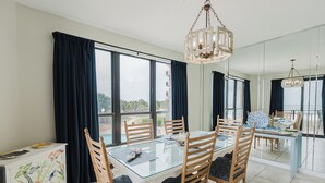 A dining area with a glass table, wooden chairs, and a chandelier. - 204E A Beautiful 3 bedroom/3 bath unit (Orange Beach)