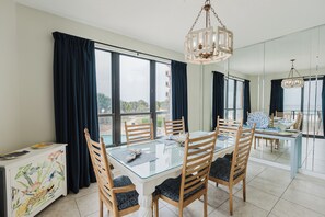 A dining area with a glass table, wooden chairs, and a chandelier. - 204E A Beautiful 3 bedroom/3 bath unit (Orange Beach)