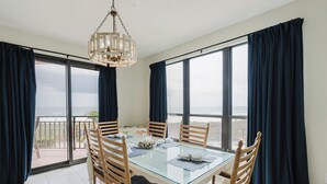 A dining area with a glass table, wooden chairs, and a view of the sea. - 204E A Beautiful 3 bedroom/3 bath unit (Orange Beach)