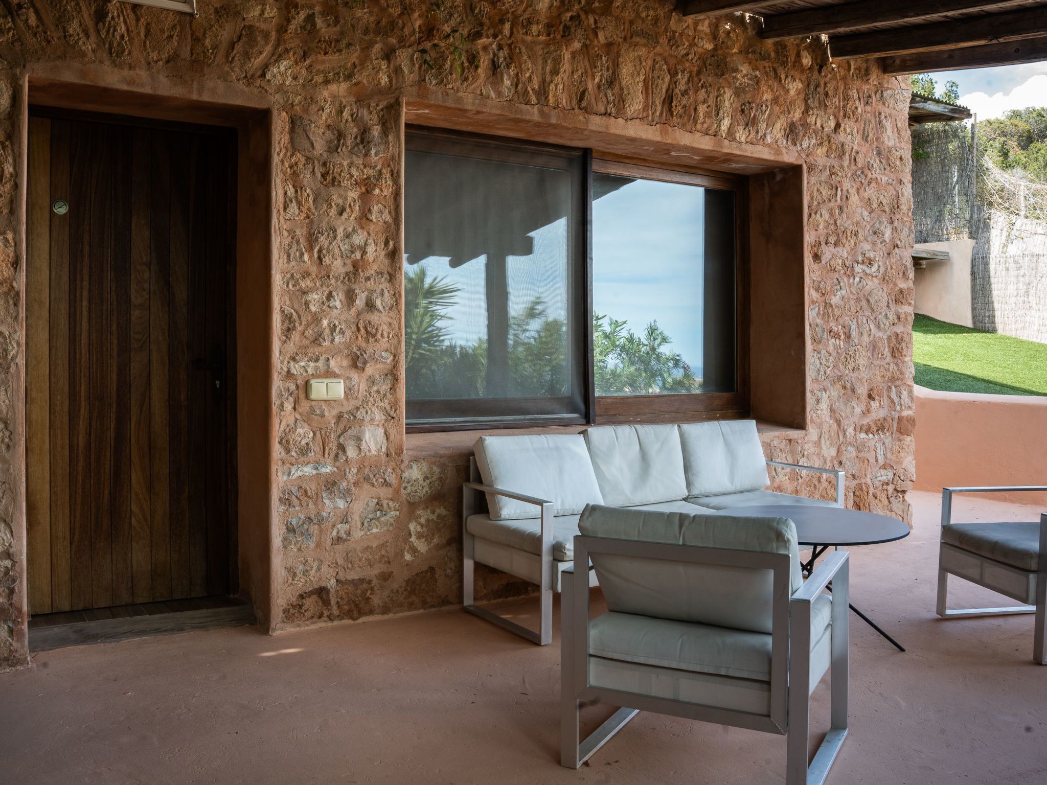 A room with a stone wall, a wooden door, a window with a view, a white sofa, and a small table.