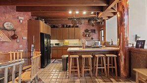 Eine Küche mit Holzausstattung, einer zentralen Kochinsel mit Hockern, hängenden Töpfen und einem gefliesten Boden.