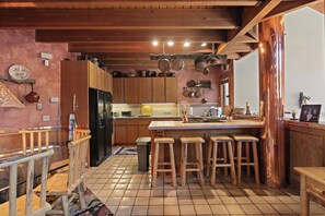 Una cocina con gabinetes de madera, una isla central con taburetes, ollas colgantes y piso de baldosas.