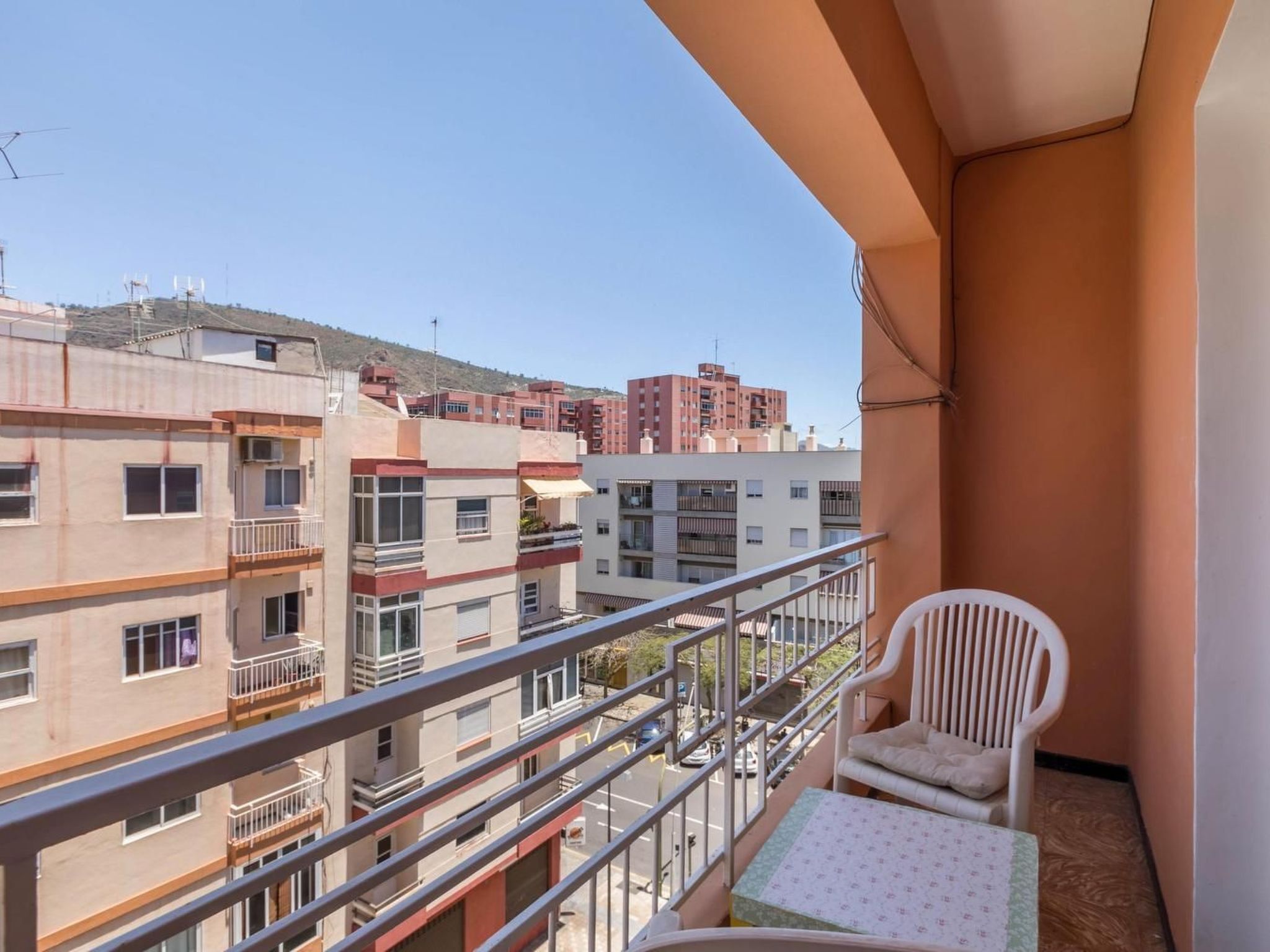 Un balcone con una sedia bianca e un tavolino, vista su una zona residenziale con edifici a più piani.