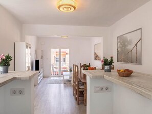 Een ruime keuken met een centraal eiland, een eethoek met een houten tafel en stoelen, en uitzicht op het balkon.